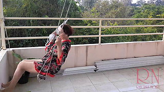 The lady is swinging on a hanging swing, hiding from the rain under an umbrella.